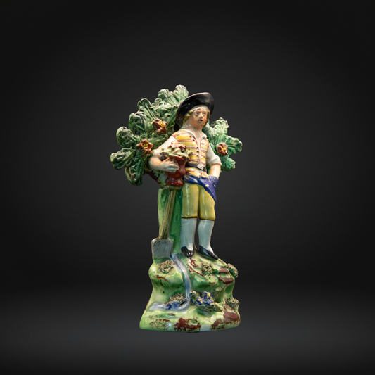 Colorful early 19th century ceramic Walton figure of a man with a basket on a dark background