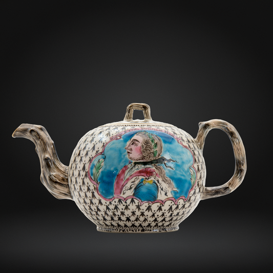 An antique Staffordshire teapot with a textured, bark-like brown spout and handle, decorated with a black-and-white diamond pattern and a central hand-painted portrait of the King of Prussia.