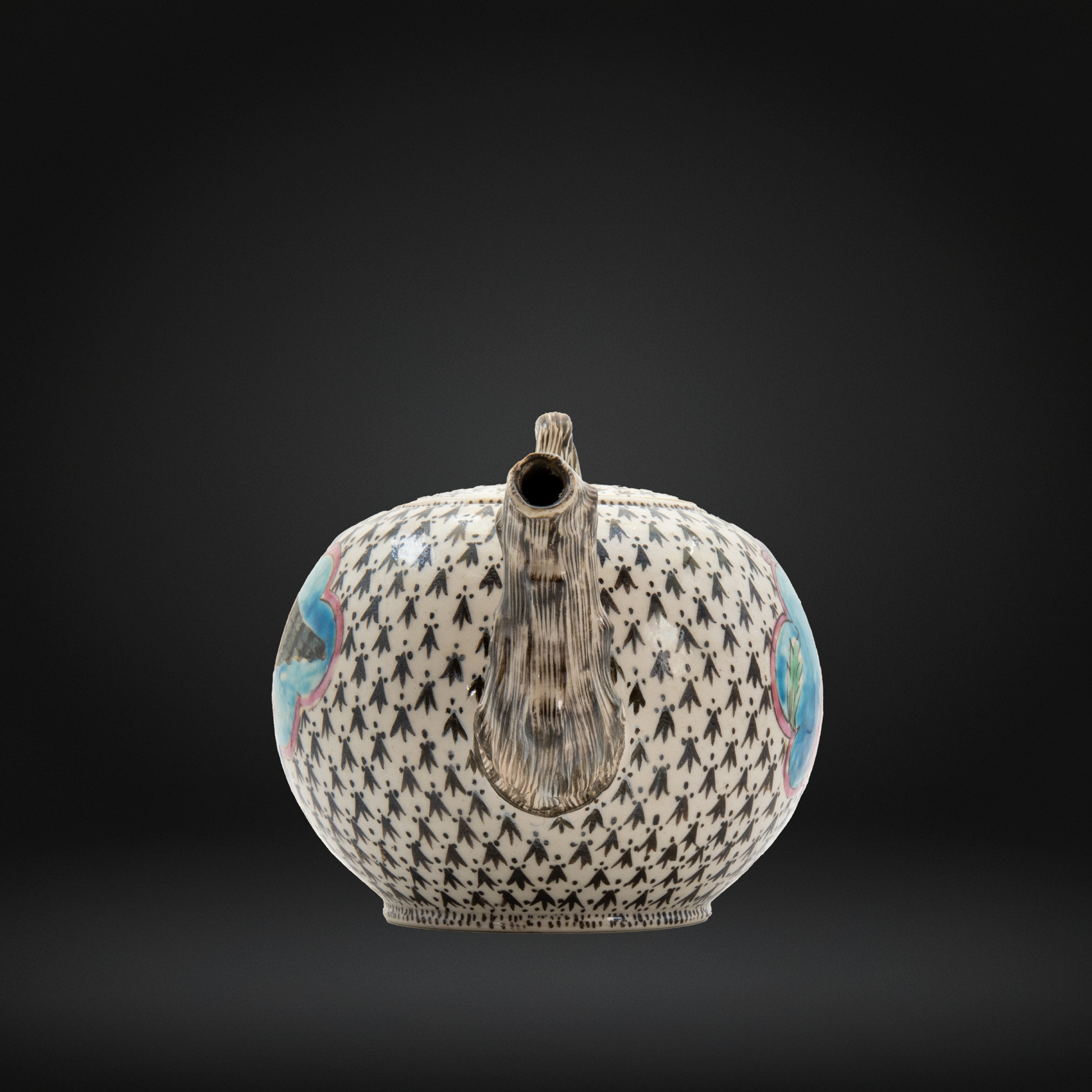 The spout of an 18th century staffordshire stoneware teapot with a black and white geometric pattern, featuring a textured brown handle and spout, with small blue and pink painted details on the sides, set against a dark gray gradient background.