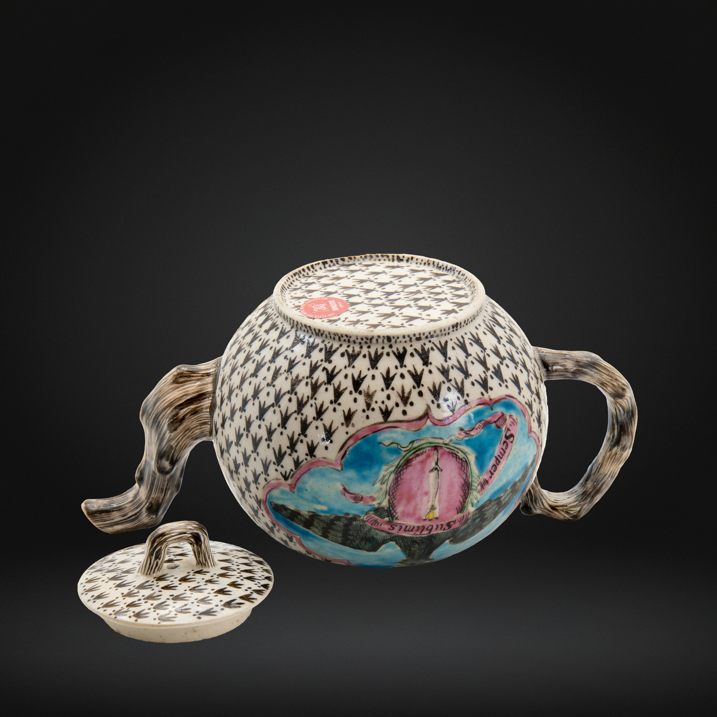 The underside of an 18th century Staffordshire teapot with a lid, featuring a black and white ermine ground pattern, a naturalistic handle and spout, and a colorful hand-painted panel.