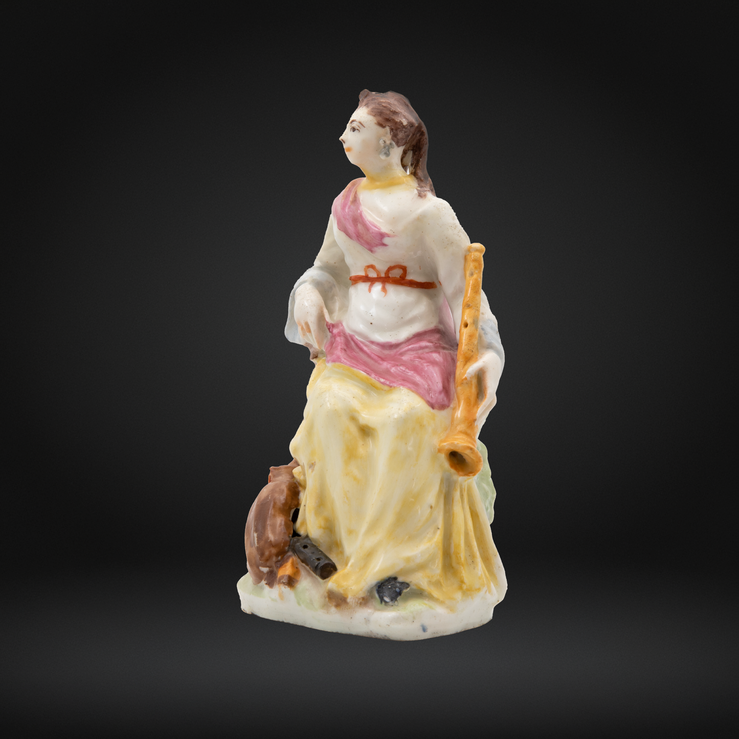 An antique porcelain figurine of a seated woman holding a musical instrument, painted in soft pastel colors of yellow, pink, and white against a dark gradient background.