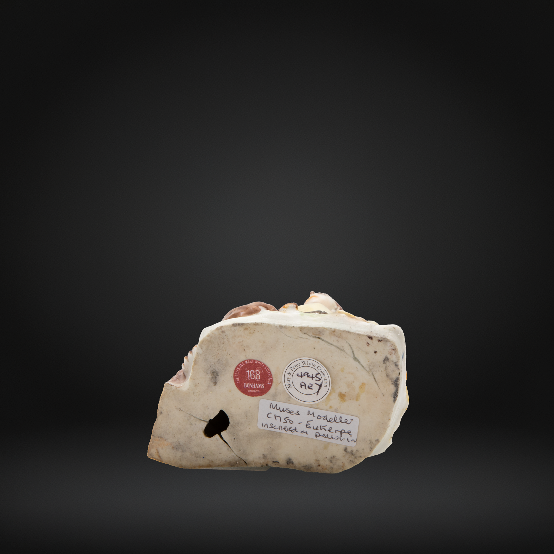 The base of an early Bow porcelain figure, featuring the collection stickers for the Peter and mary white collection and Bonhams.