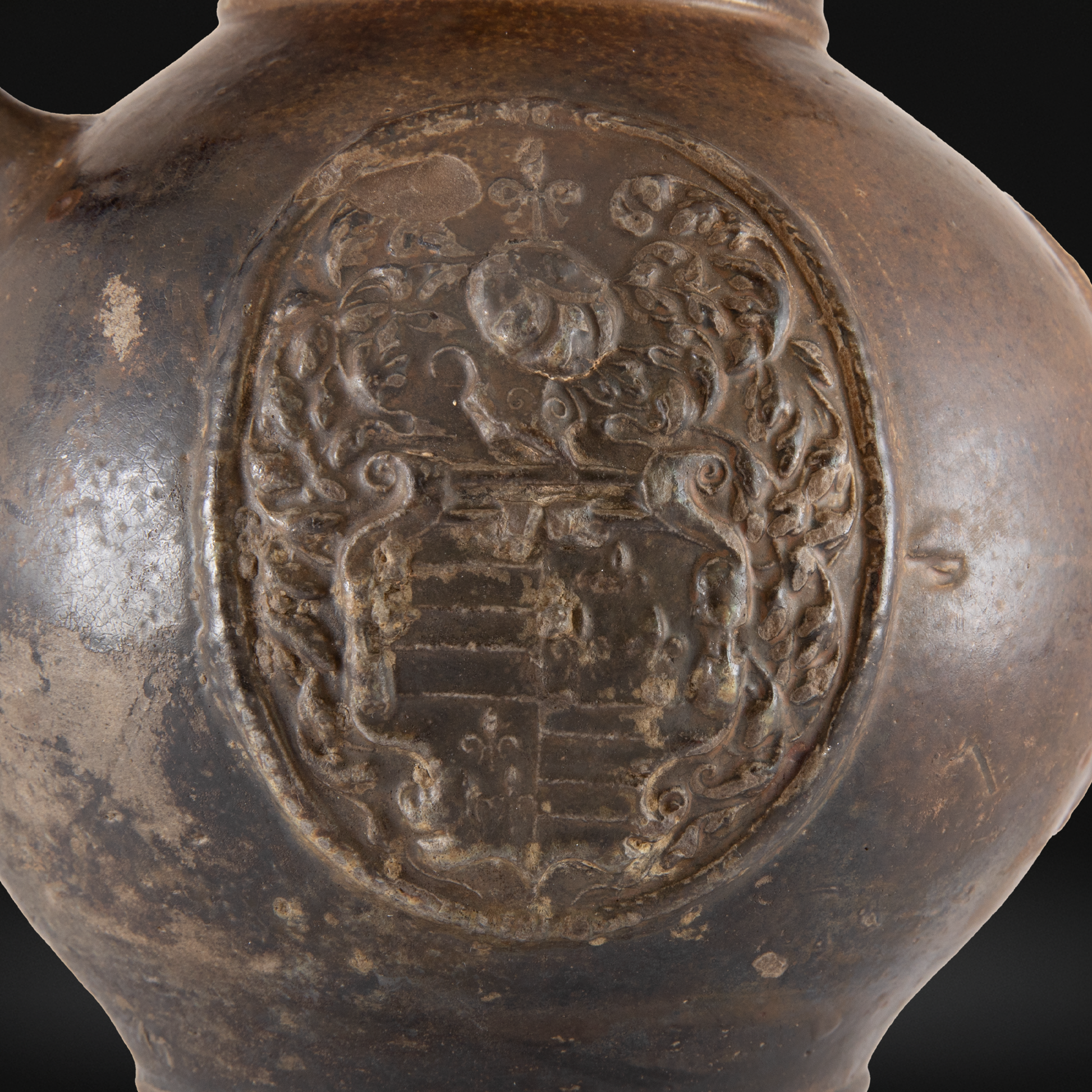 Close-up of a detailed armorial crest embossed on the surface of a 16th Century Raeren Stoneware Armorial Jug, showcasing its aged German stoneware craftsmanship.