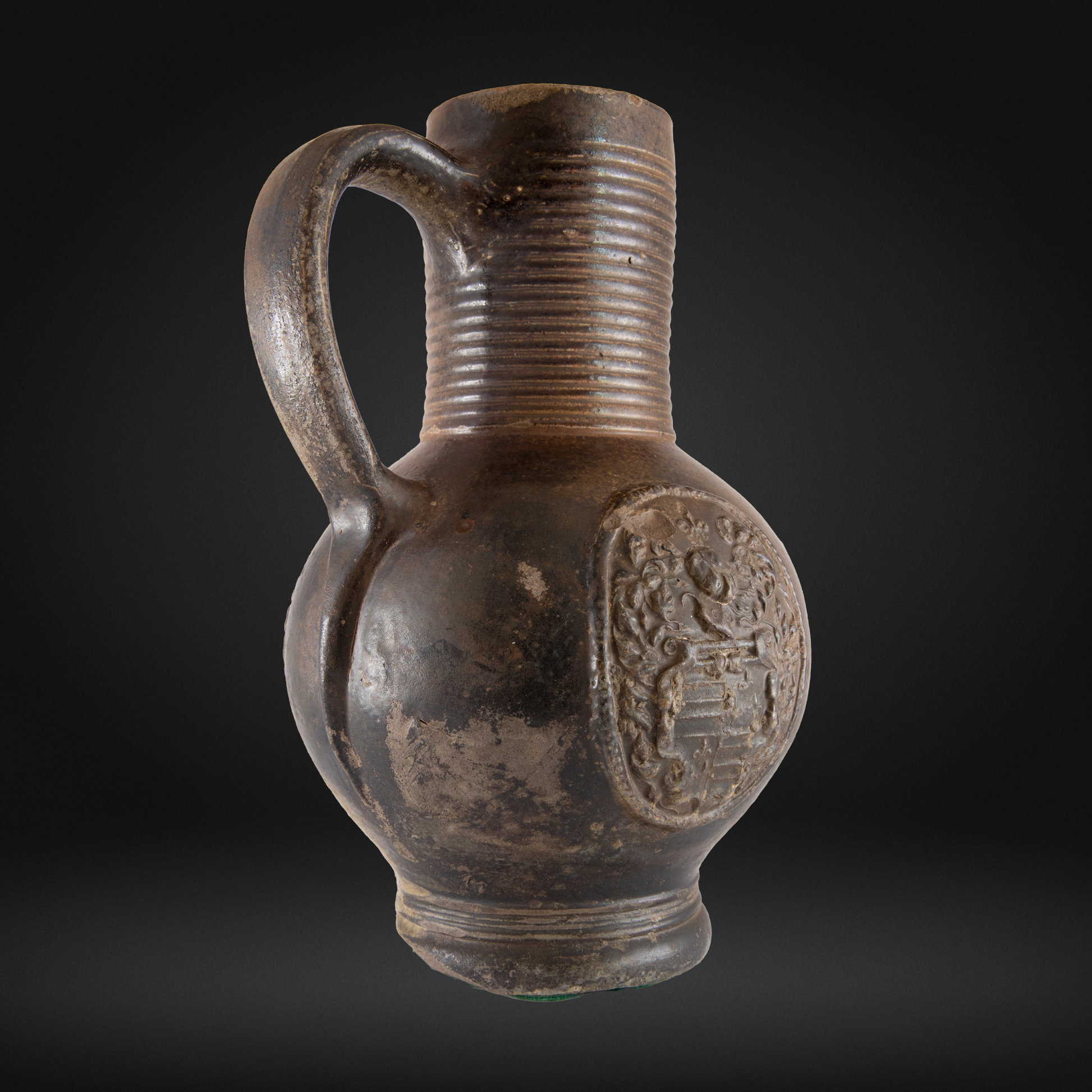 A rustic 16th Century Raeren Stoneware Armorial Jug featuring a ribbed neck and an embossed armorial coat of arms on its rounded body, showcasing antique German stoneware craftsmanship.