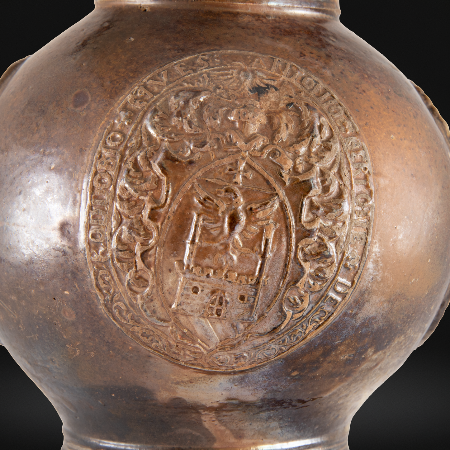 Close-up of a detailed coat of arms embossed on a brown glazed surface of a 16th Century Raeren Stoneware Armorial Jug, showcasing intricate medieval design.